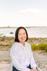 Dr. Chan pictured on a beach with sand, grass, and water behind